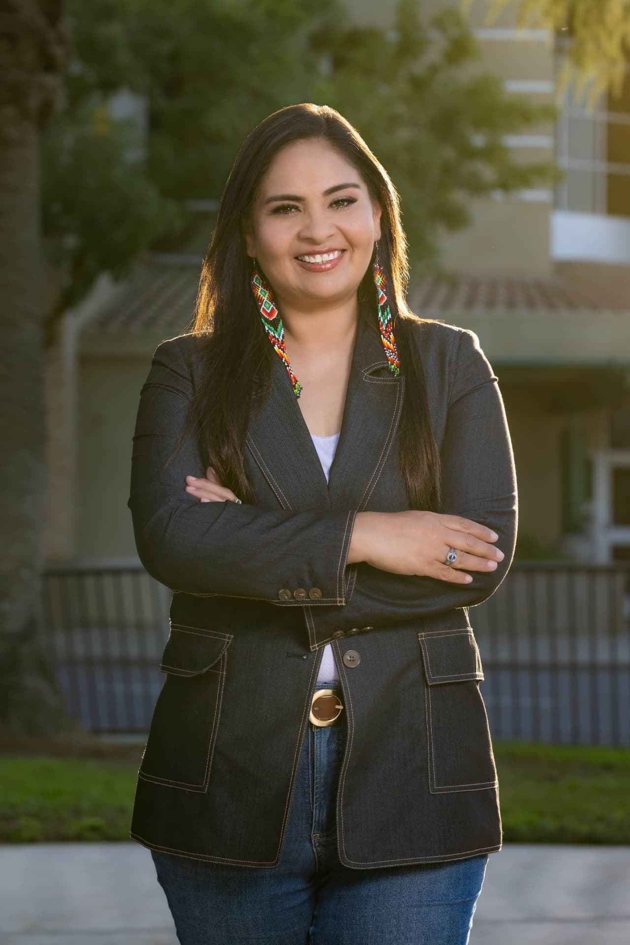 Maria Pacheco smiling with her arms crossed, wearing beaded earrings and a denim jacket